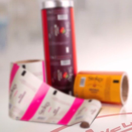 Three reels of printed laminated film — a purple coffee film, a pink label film and a yellow sachet film.